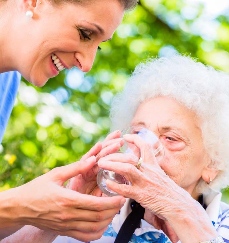 Eine Pflegerin hilft einer älteren Dame beim Trinken