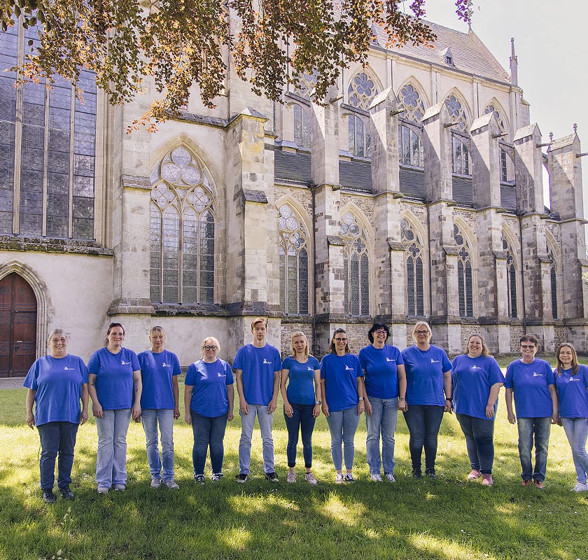 Das Pflegeteam der Aktiv Pflege Odenthal in blauen T-Shirts vor dem Altenberger Dom